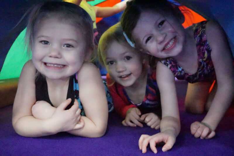 Three young girls smiling and playing under gymnastics donut