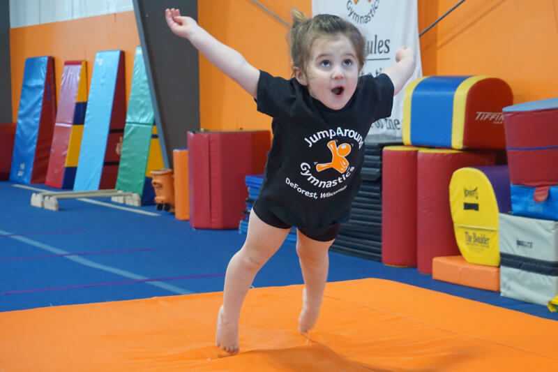 Young girl having fun jumping onto gymnastics landing mat