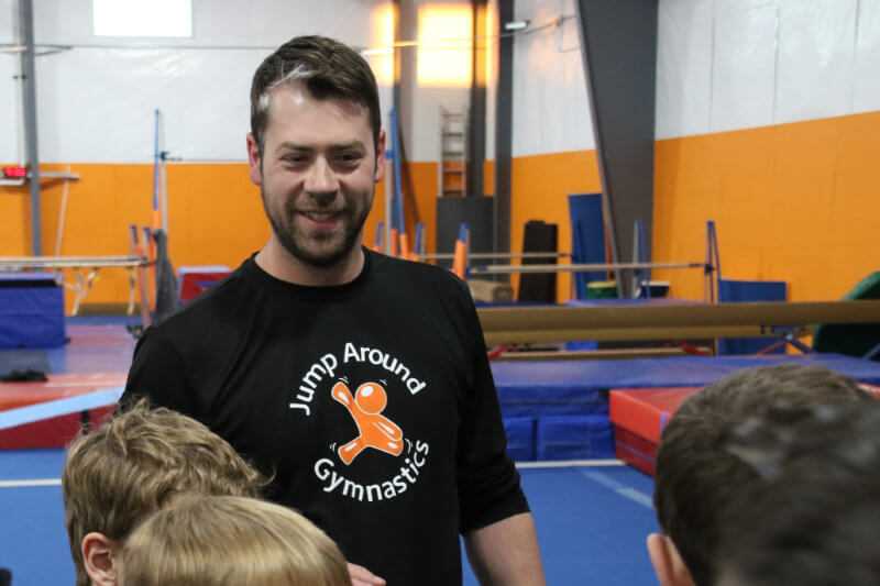 Coach and owner Ben O'Neill smiling and giving pep talk to team at a gymnastics competition